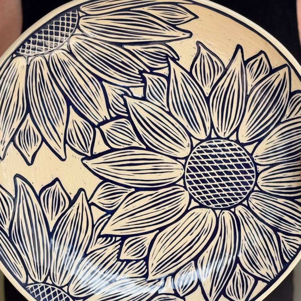 A round stoneware platter carved with a large navy-blue sunflower on an off-white background